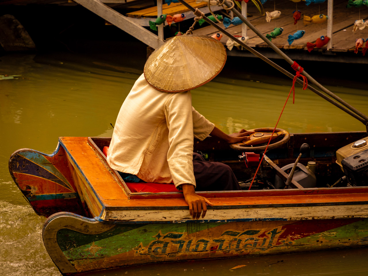 Boatman wearing a straw hat paddling a boat through a floating market in Thailand.
