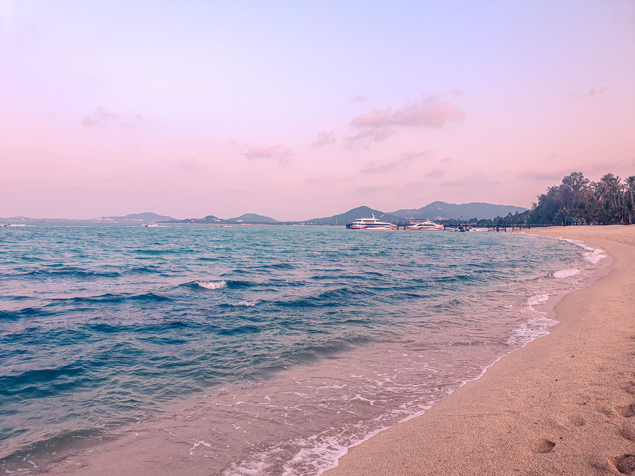 Sandy beach and sea with yachts in the distance at sunset on Koh Samui, Thailand.